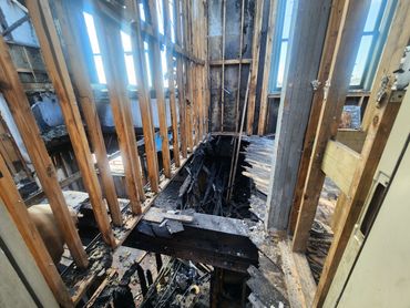Interior of a fire-damaged building with exposed wooden beams and charred debris.