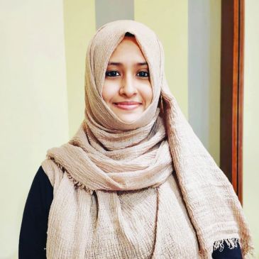Smiling woman wearing a beige hijab and black top.