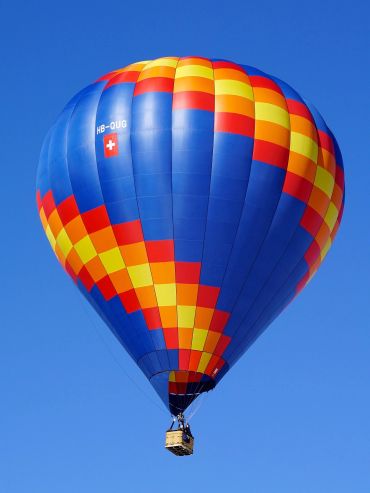 Colorful hot air balloon with red, yellow, and blue patterns floating against a clear blue sky.
