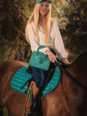 Woman in teal accessories sitting on a horse with brown fur.