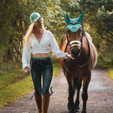 Woman in casual attire walking with a brown horse in a green forest path.