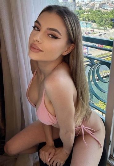 Young woman in pink bikini posing by a balcony.
