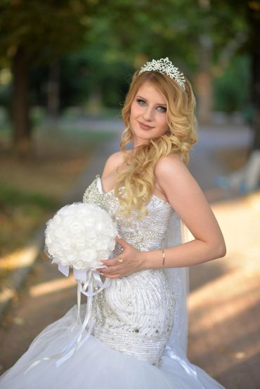 Bride in an elegant white gown holding a bouquet of white roses.