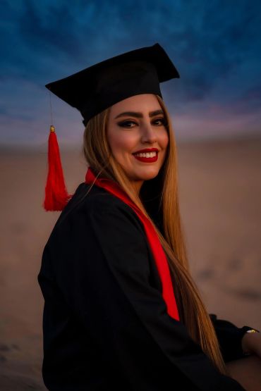 Smiling graduate woman in cap and gown at sunset.