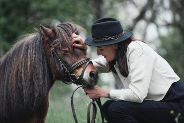 A woman affectionately caresses a pony outdoors.