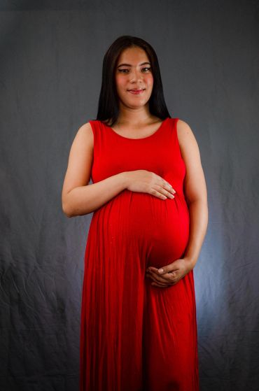 Pregnant woman in a red dress smiling gently.