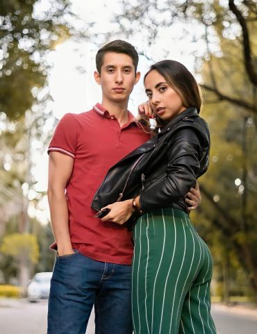 Young couple posing confidently outdoors with blurred trees in background.