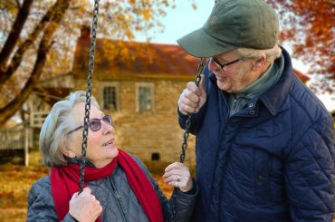 Elderly couple sharing a joyful moment on a swing in autumn.