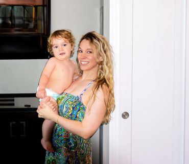 Smiling woman holding a baby in a colorful dress indoors.