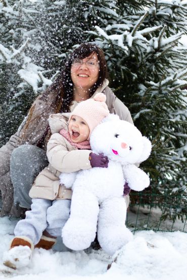 A happy child and woman in winter clothes play in the snow with a large white teddy bear.