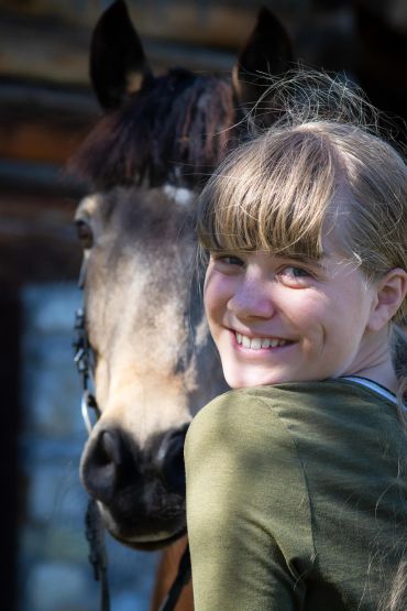 Smiling girl posing with a horse in sunlight.