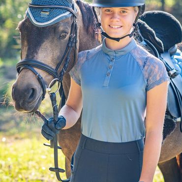 Young woman in equestrian gear standing beside her horse outdoors.