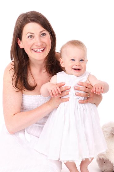 Happy mother and baby dressed in white, smiling together.