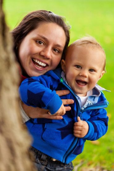 A happy mother and baby smiling outdoors with green background.
