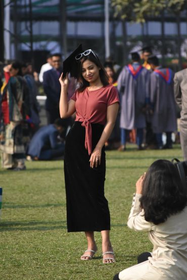 A young woman posing with a graduation cap at an outdoor ceremony.