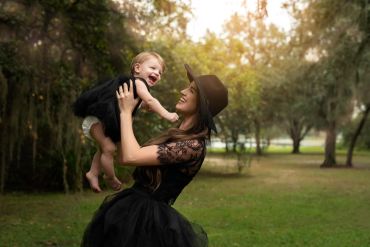 A joyful mother lifts her laughing baby outdoors in matching black outfits.