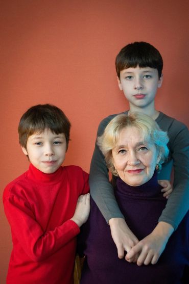 Grandmother with her two grandsons posing against a warm orange background.