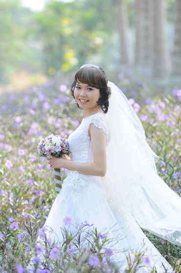 Smiling bride in white dress holding bouquet among purple flowers.