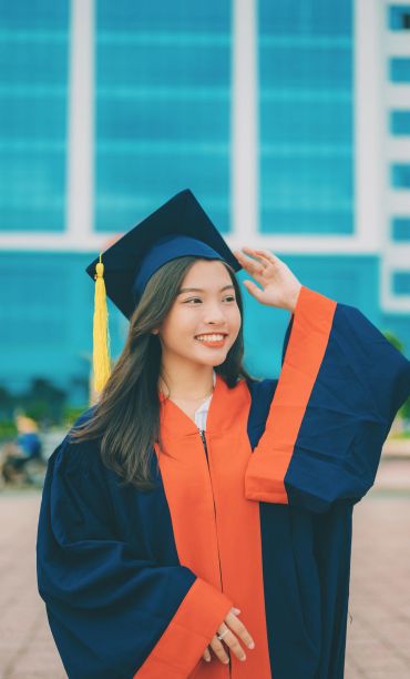 Smiling female graduate in cap and gown with yellow tassel.