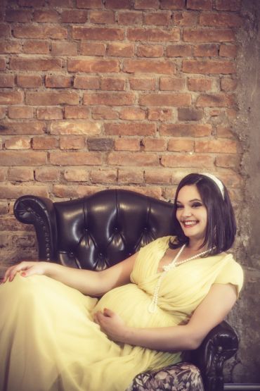 Smiling pregnant woman in a yellow dress sitting on a leather armchair.