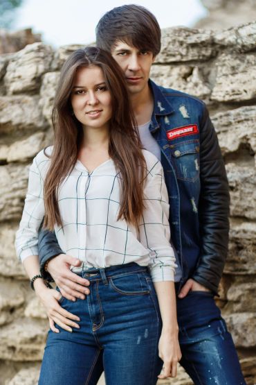 Young couple posing closely outdoors against a stone wall.