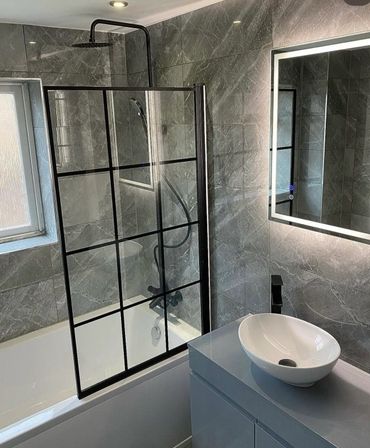 Modern bathroom with gray marble tiles, black-framed glass shower screen, and illuminated mirror.