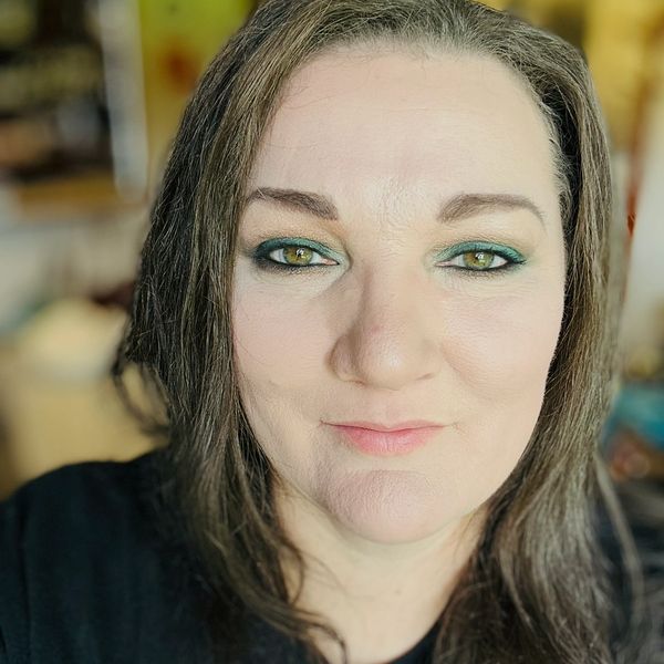 Close-up of a woman with green eye makeup and a gentle smile.