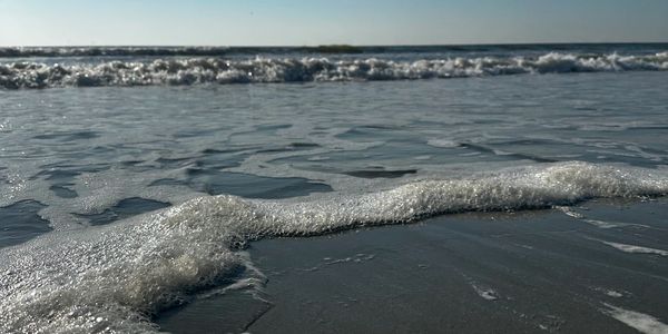 Close-up of ocean waves gently washing ashore under a clear sky.