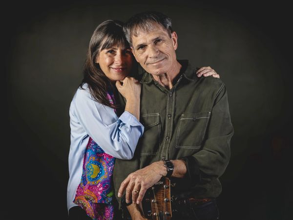 A couple posing closely, smiling with affection against a dark background.