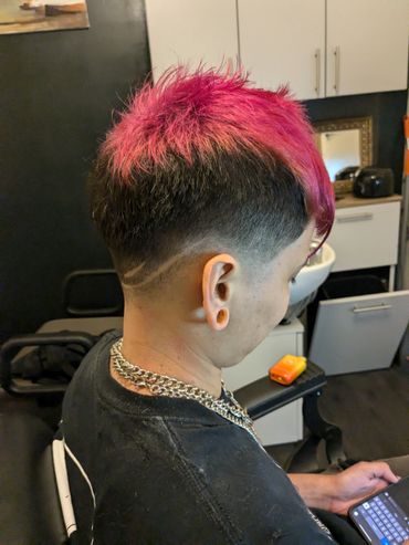 Person with vibrant pink spiky hair and a design shaved into the fade.