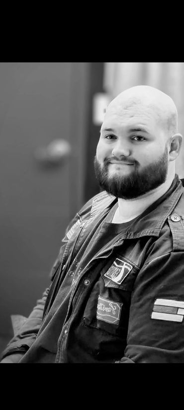 Smiling man with a beard in a jacket sitting indoors.