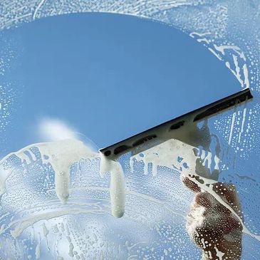 Hand cleaning a glass window with a squeegee and soap.
