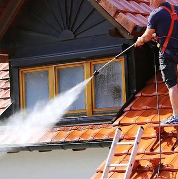 Man power washing a tiled roof near a dormer window.