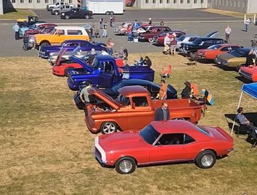 A lineup of classic cars and trucks at an outdoor car show with people admiring them.