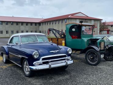 Two vintage cars, a blue Chevrolet and a green tow truck, parked side by side.