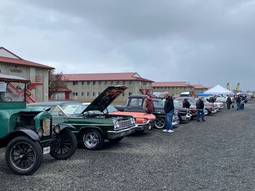 A lineup of classic cars at an outdoor car show on a cloudy day.