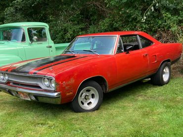 Red vintage muscle car parked on grass beside a green classic truck.