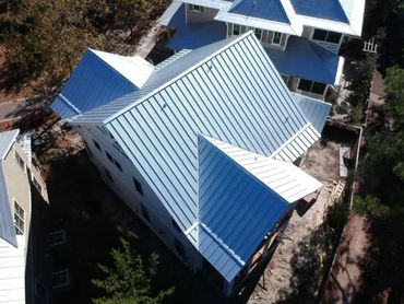 Aerial view of a house with a shiny metal roof in a residential area.
