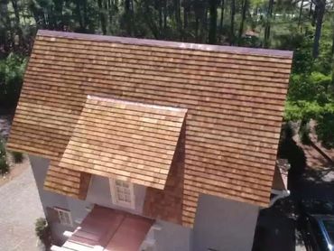 A house with a brown shingle roof surrounded by trees.