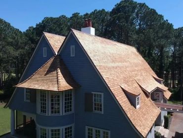 A large blue house with a uniquely shaped wooden roof under a clear blue sky.