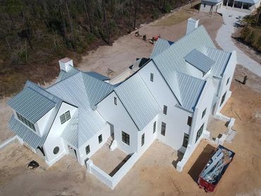 Aerial view of a large white house with a metal roof under construction.