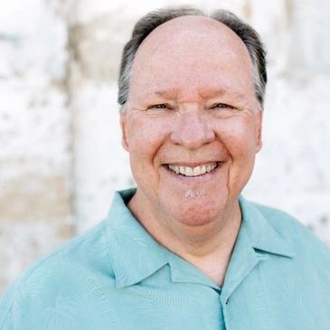 Smiling middle-aged man in a teal shirt against a light background.