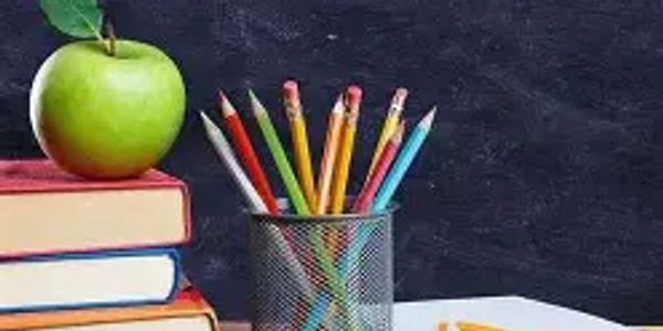A green apple on books with pencils in a holder against a blackboard.