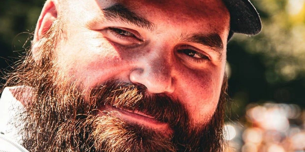 Close-up of a bearded man smiling warmly in natural light.