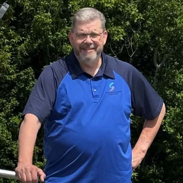 Man smiling outdoors in a blue shirt.