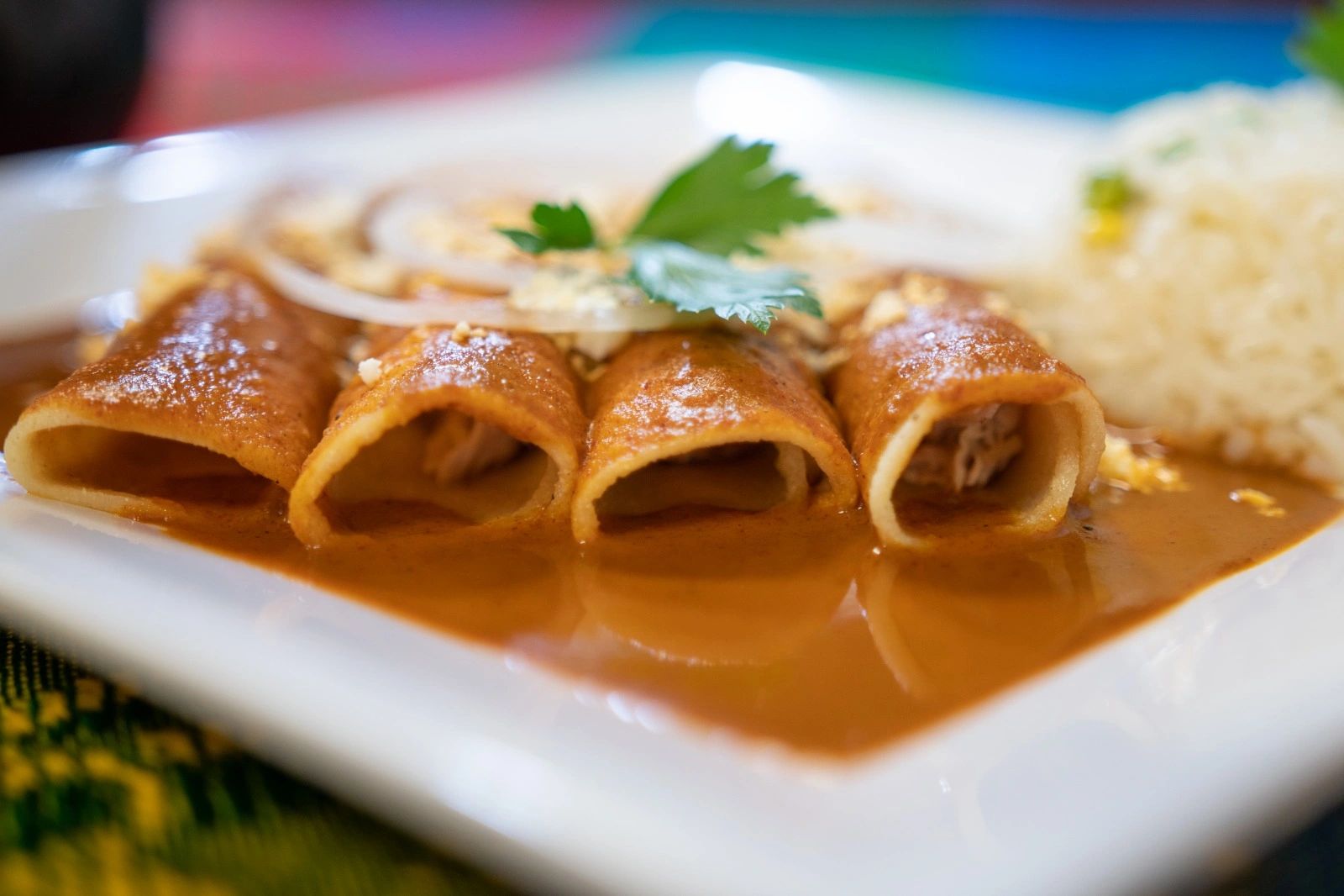 Rolled corn tortilla covered with Mole sauce onions and white rice on the side