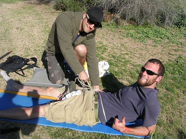 Man helps another man with a rope outdoors.