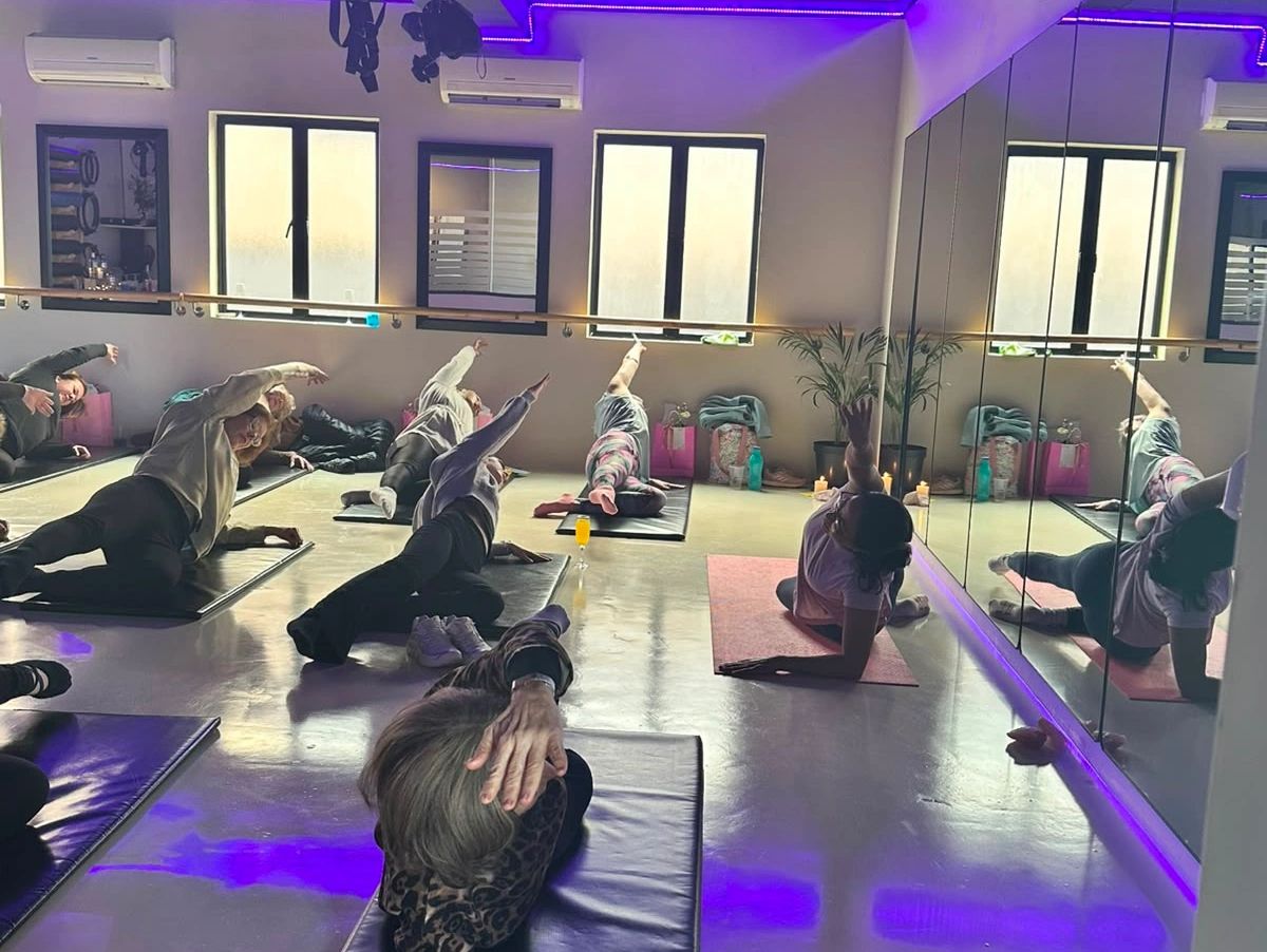 Group yoga class stretching side body on mats in studio with purple lighting.