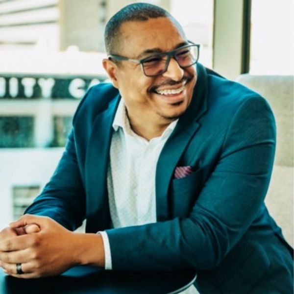 A handsome man with glasses and a blue suit smiling in a candid photo.