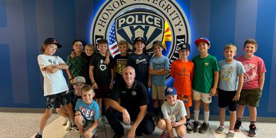 Group of kids with a police officer posing in front of a police emblem.